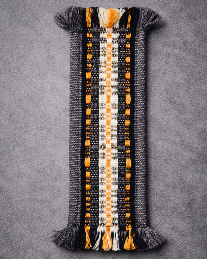 Detail eines handgewebten Lesezeichens von Wiedengold mit geometrischer Struktur.