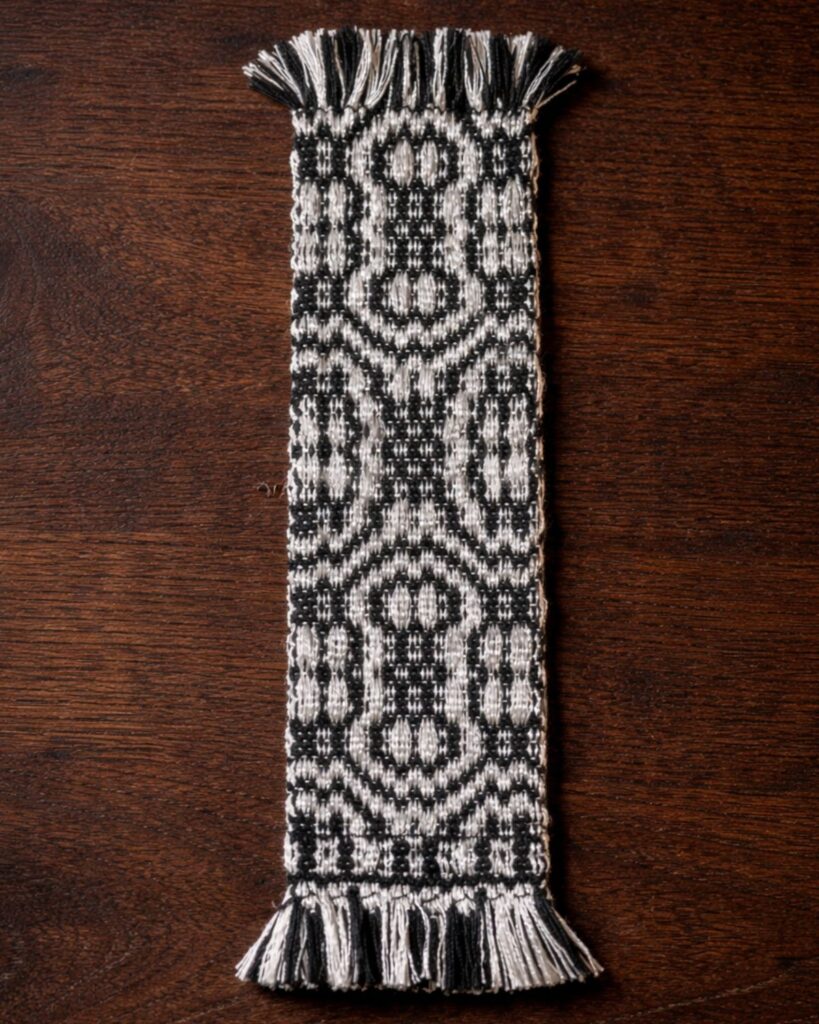Detail eines handgewebten Lesezeichens von Wiedengold mit schwarzem Ornamentmuster.
