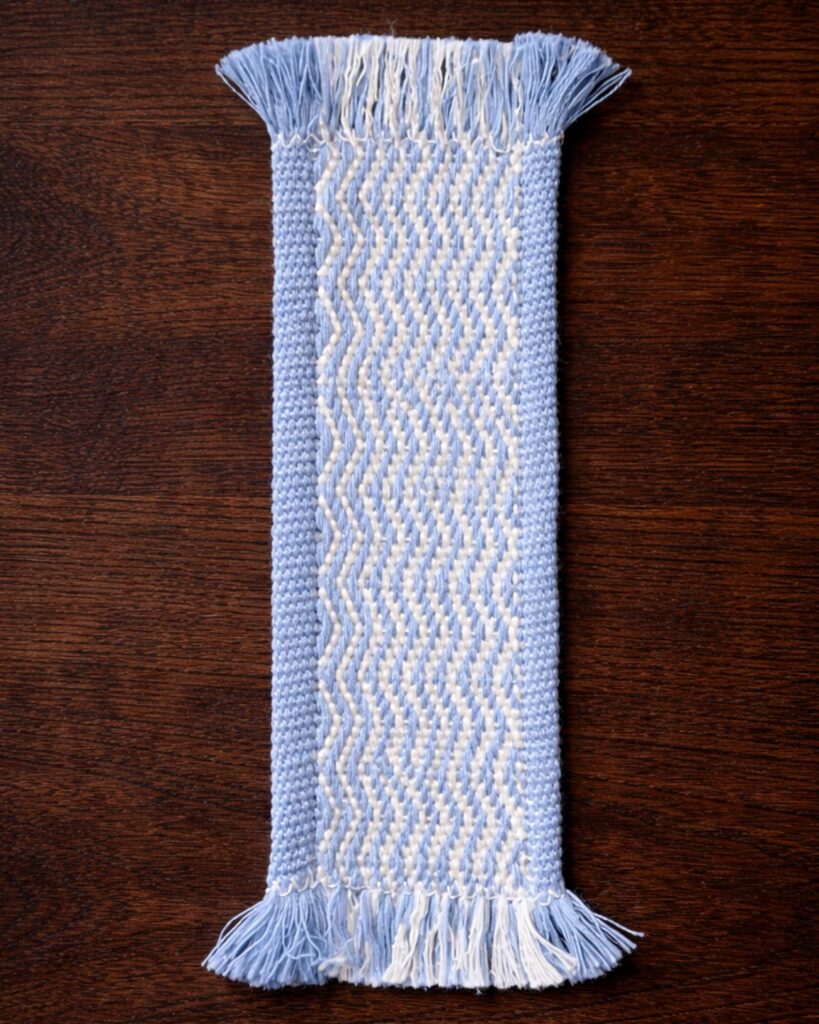 Detail eines handgewebten Lesezeichens von Wiedengold mit blauem Wellenmuster.