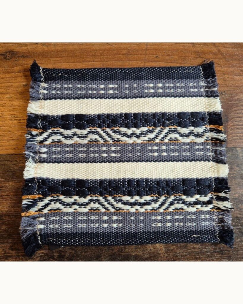 Detailansicht eines handgewebten Untersetzer von Wiedengold aus Wolle und Viskose mit Streifenstruktur in Blau und Weiß.