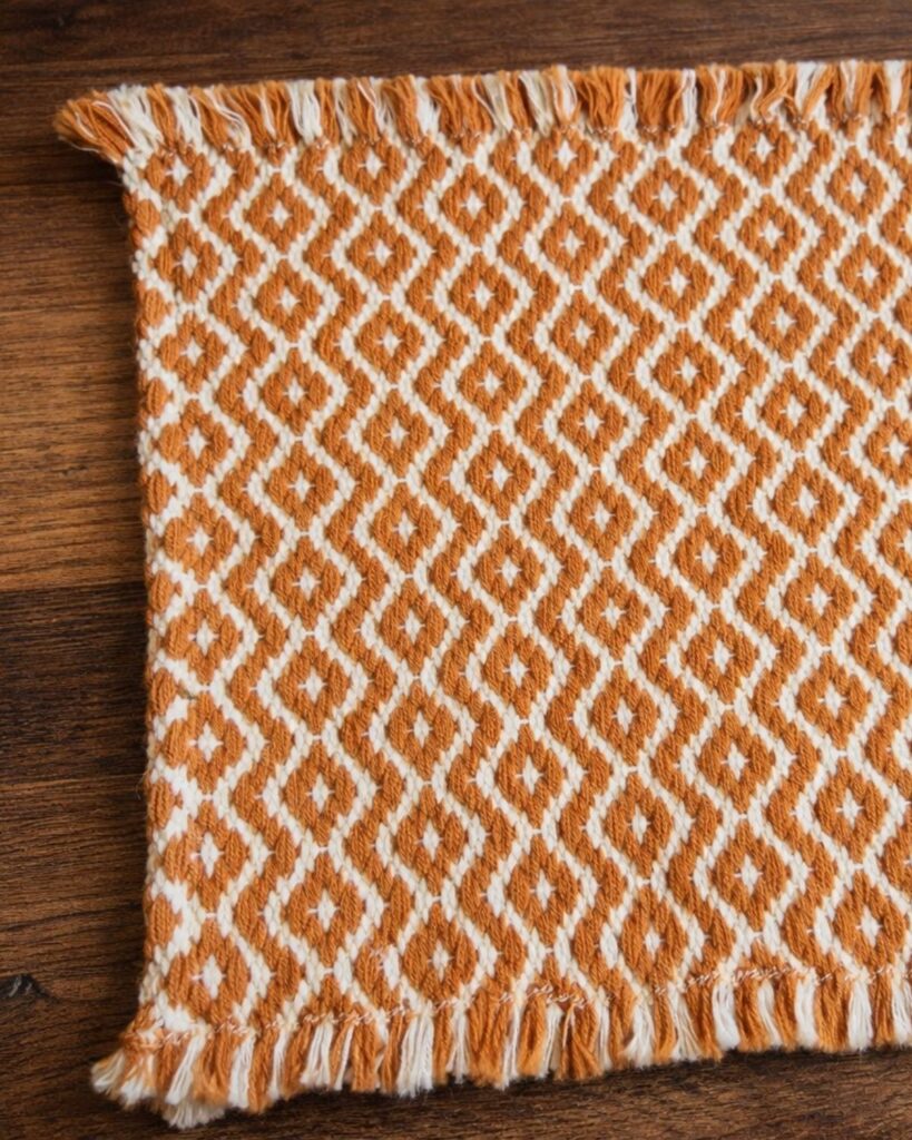 Detailansicht eines handgewebten Untersetzers aus Wolle mit geometrischem Muster.