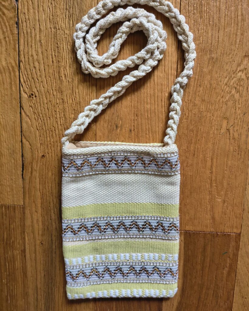 Handgewebte Handtasche aus Naturmaterialien in Creme und Gold mit ornamentaler Borte mit Goldakzenten.