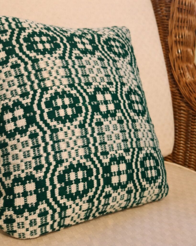 Detailaufnahme eines handgewebten Kissens mit ornamentaler Struktur in Tannengrün und Weiß.