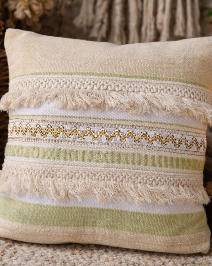Detailaufnahme eines handgewebten Kissens mit Fransen, Zierborte und goldfarbenen Akzenten in Creme und Hellgrün.