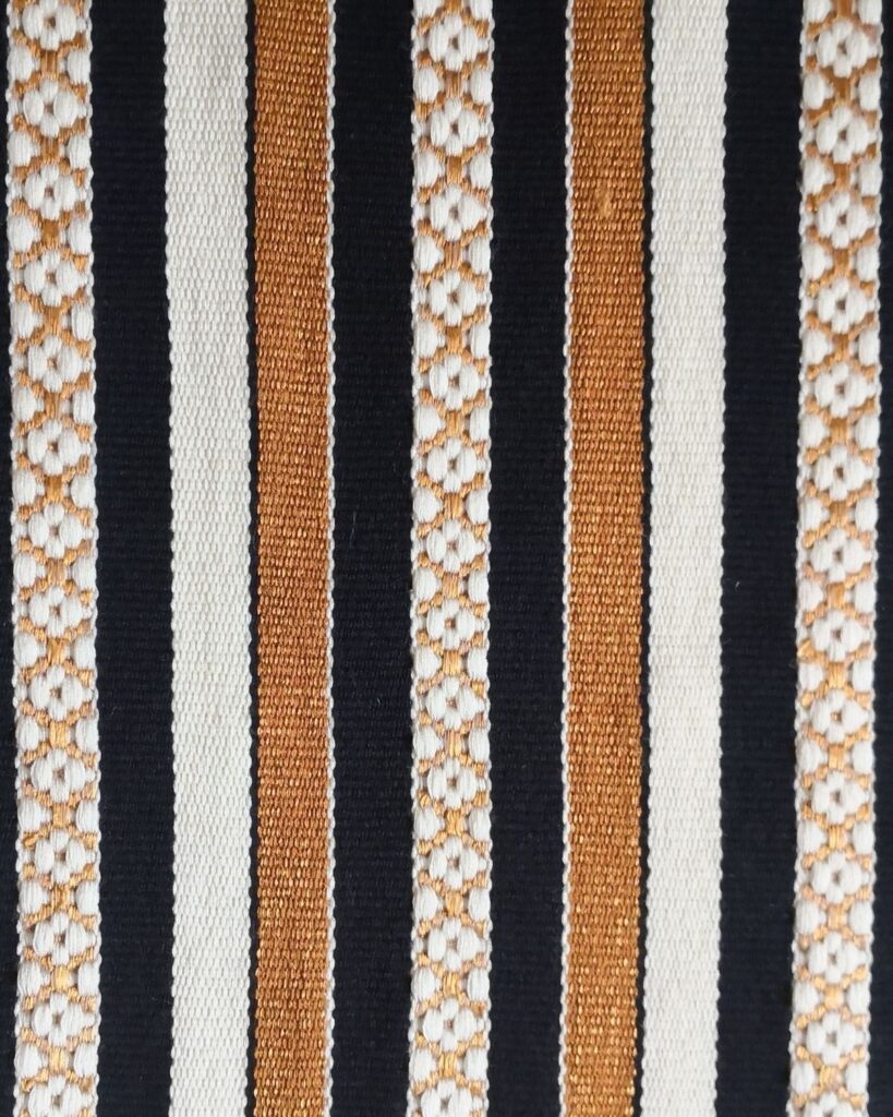 Detailaufnahme eines handgewebten Webstoffes aus Wolle und Viskose mit Streifen in Gold, Schwarz und Weiß.