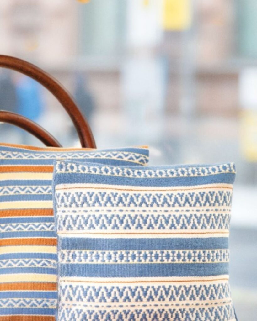 Handgewebte Kissen mit Streifen in Blau, Weiß und Ocker auf klassischem Holzstuhl.