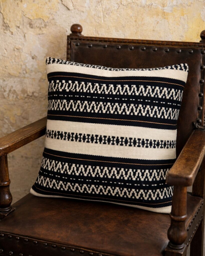Handgewebtes Kissen von Wiedengold mit grafischer Streifenstruktur in Schwarz und Weiß auf antikem Sessel mit Lederlehne.
