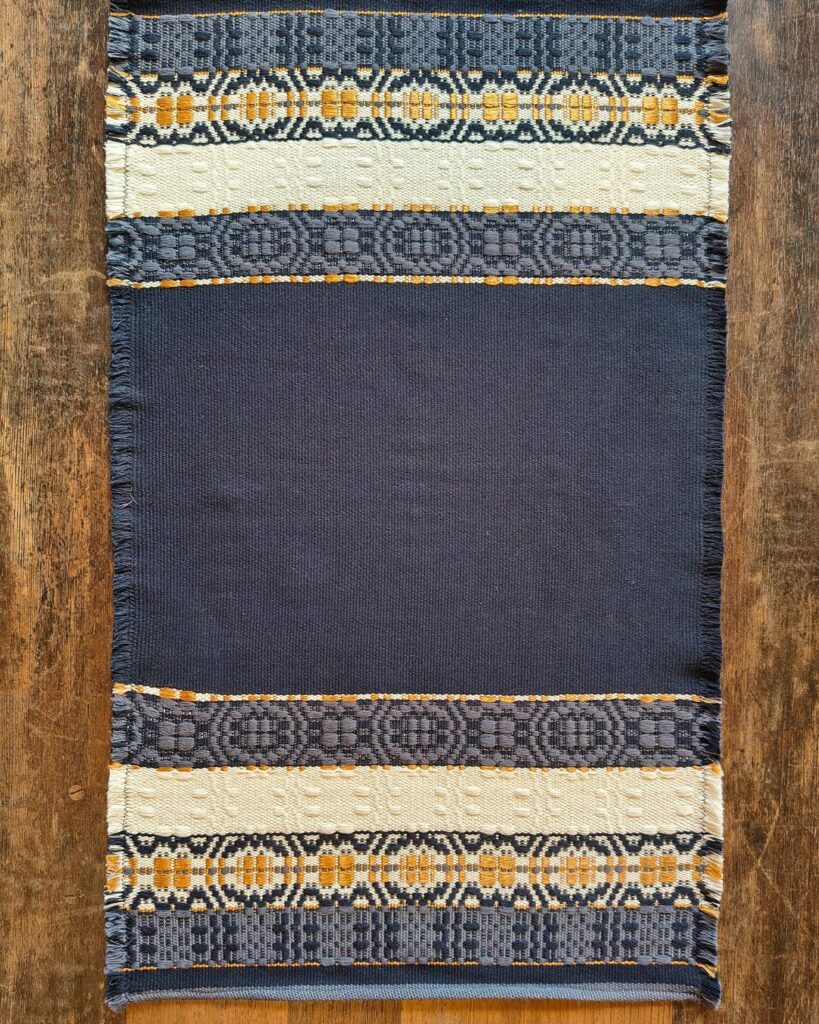 Detail eines handgewebten Wandbehangs von Wiedengold in Dunkelblau, Gold und Weiß.