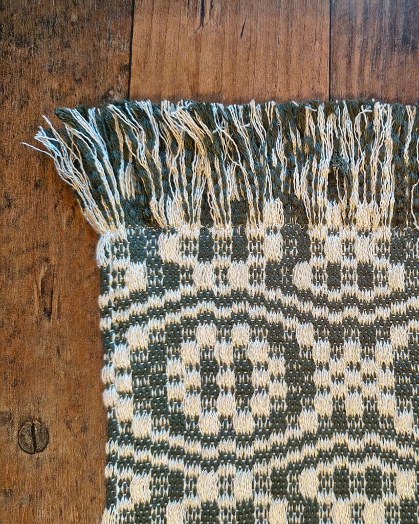 Detailaufnahme eines handgewebten Tischläufers von Wiedengold in Grün und Weiß mit ornamentaler Struktur und Fransen.