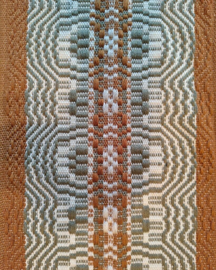 Detailansicht eines handgewebten Tischläufers aus Wolle von Wiedengold mit ornamentaler Struktur in Olivgrün, Ocker und Weiß.