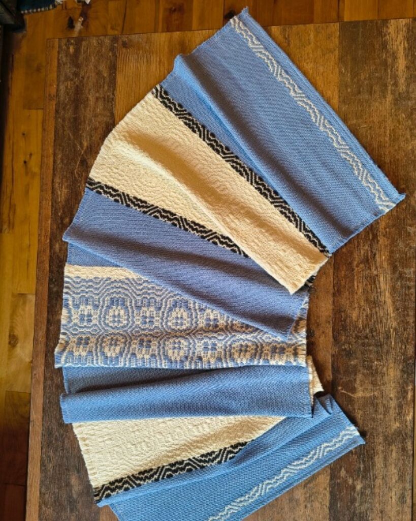 Detailansicht der Webstruktur eines handgewebten Tischläufers aus Wolle mit blauen und weißen Ornamentstreifen.