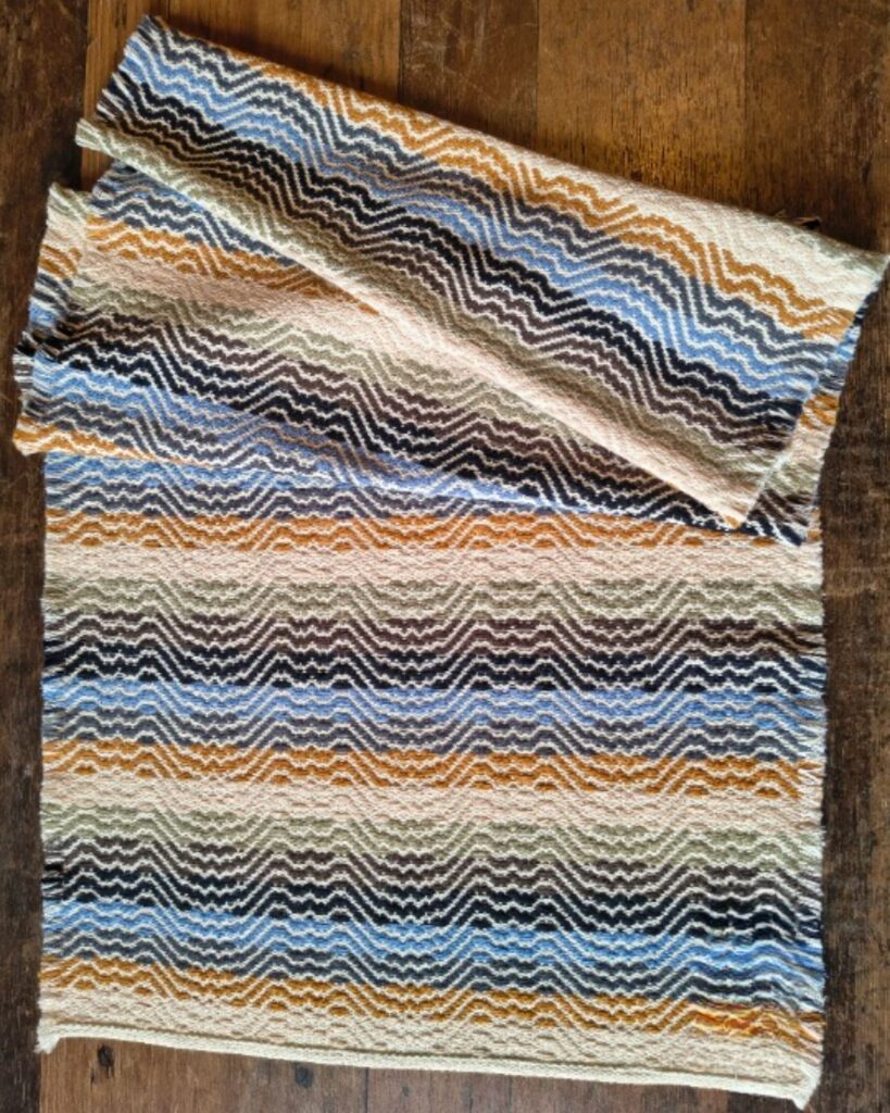 Handgewebter Tischläufer aus Wolle von Wiedengold mit wellenförmigen Streifen in Blau, Ocker und Rosa.
