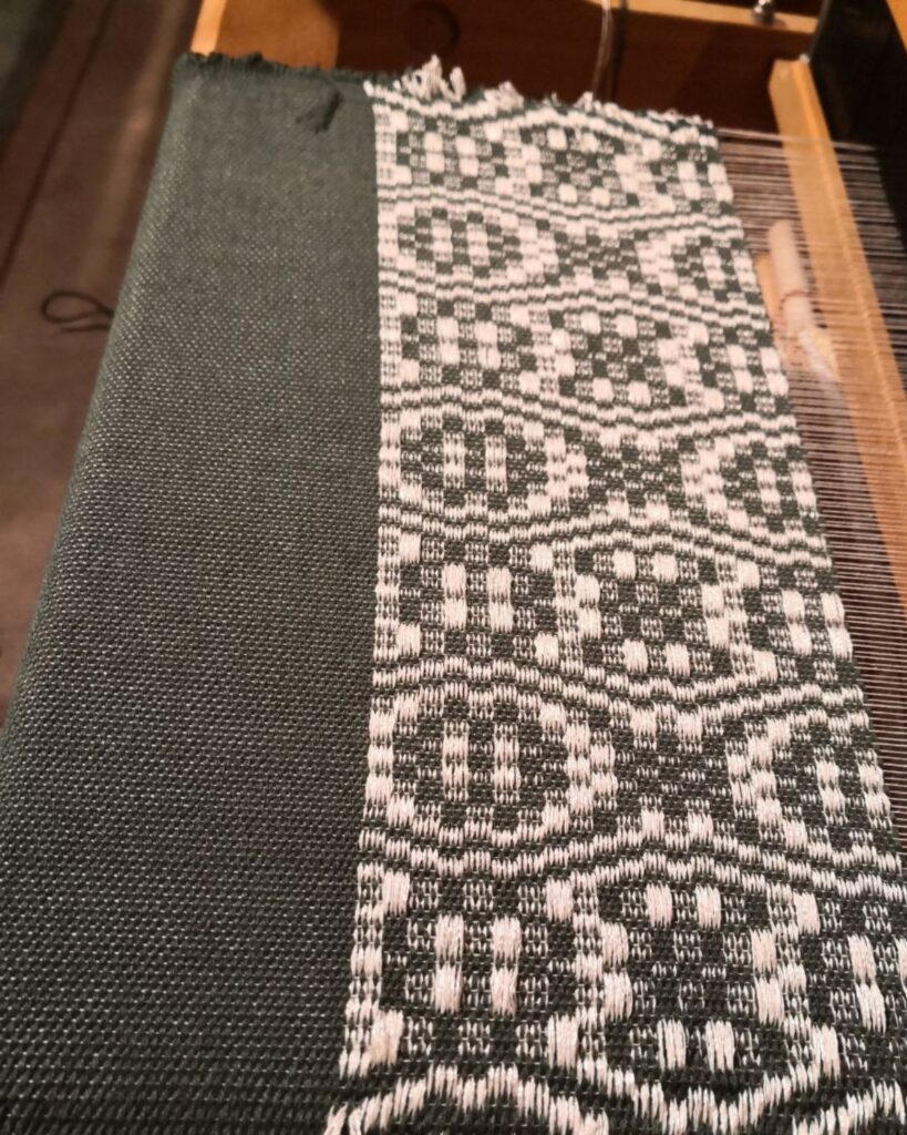 Handgewebte Webprobe mit ornamentaler Struktur in Grün und Weiß am Webstuhl von Wiedengold.