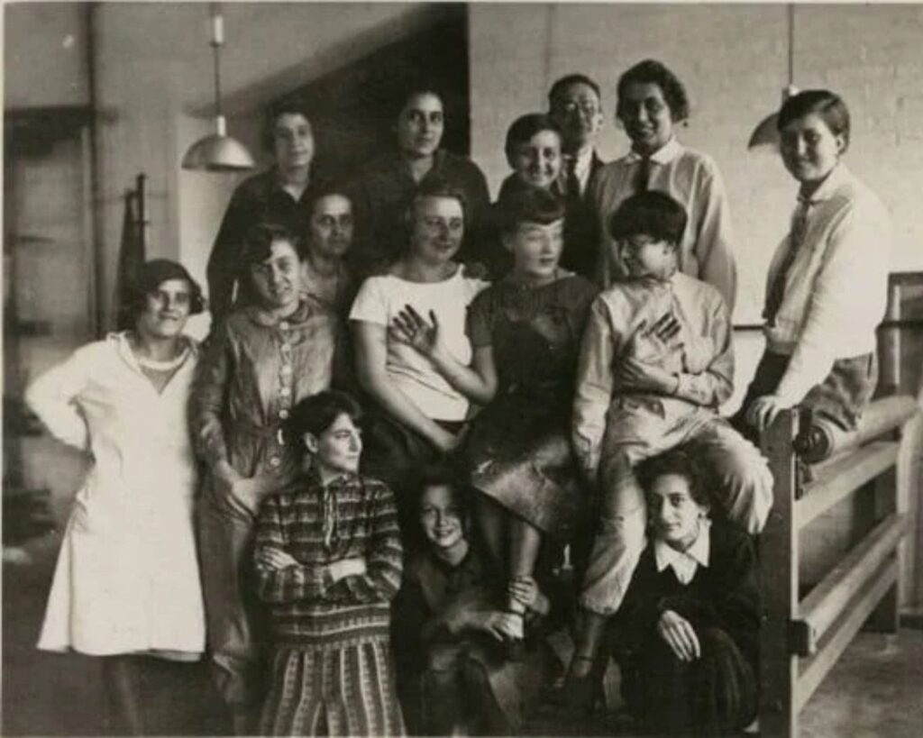 Gruppenaufnahme junger Frauen und Studierender der Bauhaus-Weberei in einem Werkraum der 1920er Jahre.