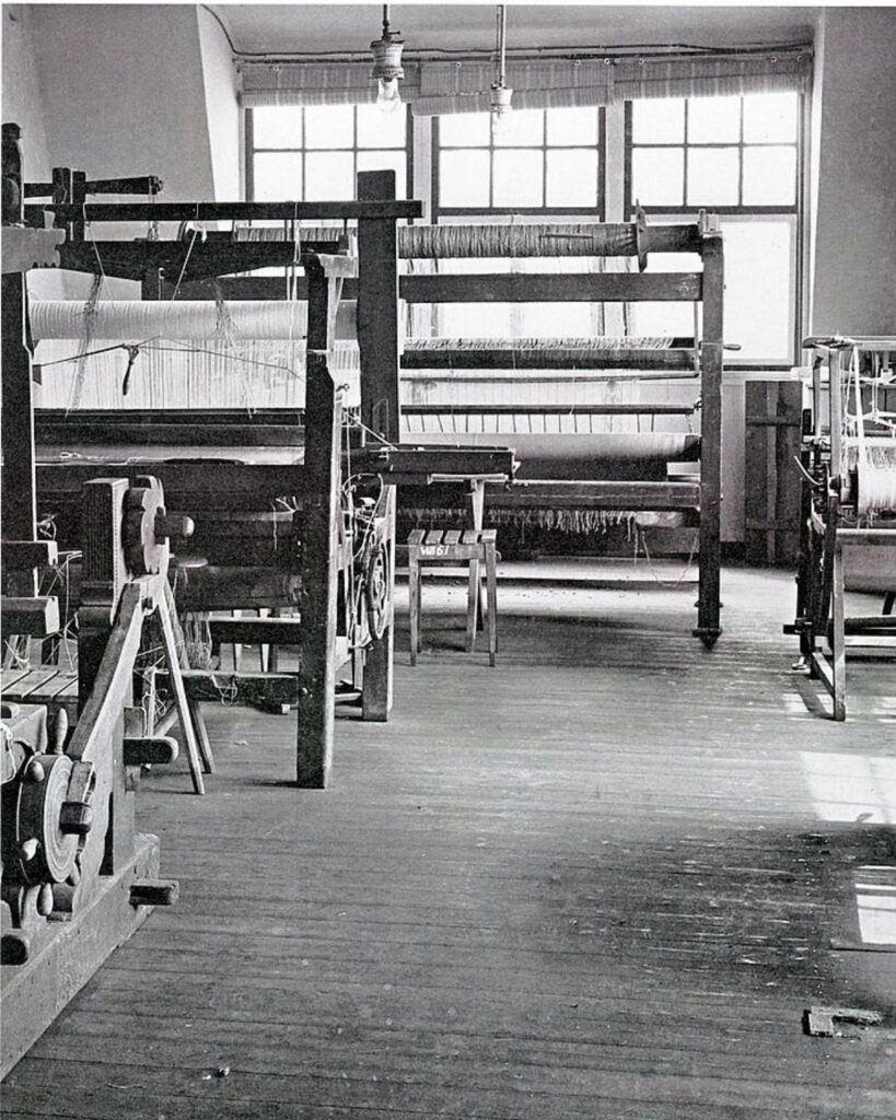 Innenaufnahme einer Bauhaus-Weberei mit mehreren Webstühlen und großen Fenstern im Hintergrund.