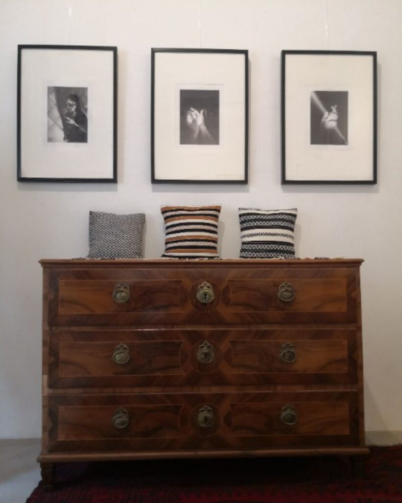 Handgewebte Kissen auf Kommode unter gerahmten Grafiken in Ausstellung.