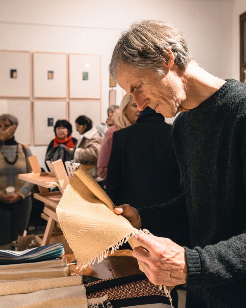 Besucher betrachtet handgewebtes Textil von Wiedengold bei Ausstellung in Graz 2025.