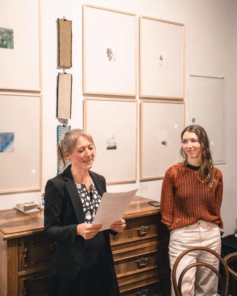 Einführung zur Ausstellung in einem Raum mit gerahmten Arbeiten und handgewebten Stoffmustern an der Wand.