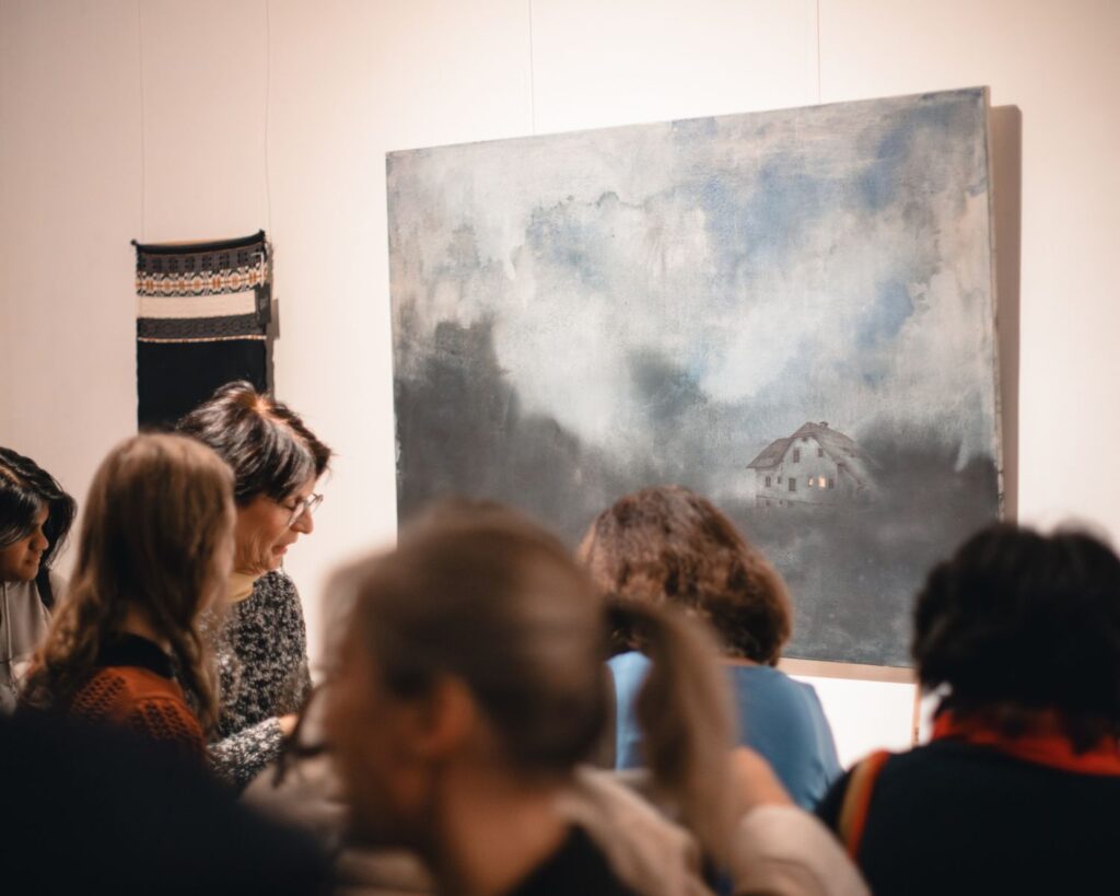 Gäste vor Gemälde und Textilarbeit beim Pop-up Kunstmarkt in Graz 2025 von Mirjam Schrei und Sandra Wiedner, Boutique-Weberei Wiedengold.