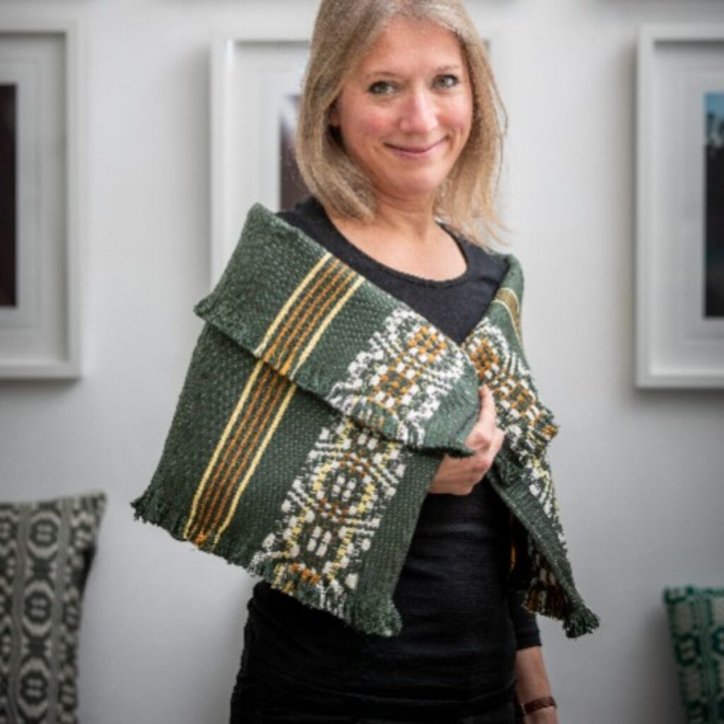 Handweberin der Boutique-Weberei Wiedengold mit handgewebtem Schultertuch in Grün, Ocker und Naturtönen.