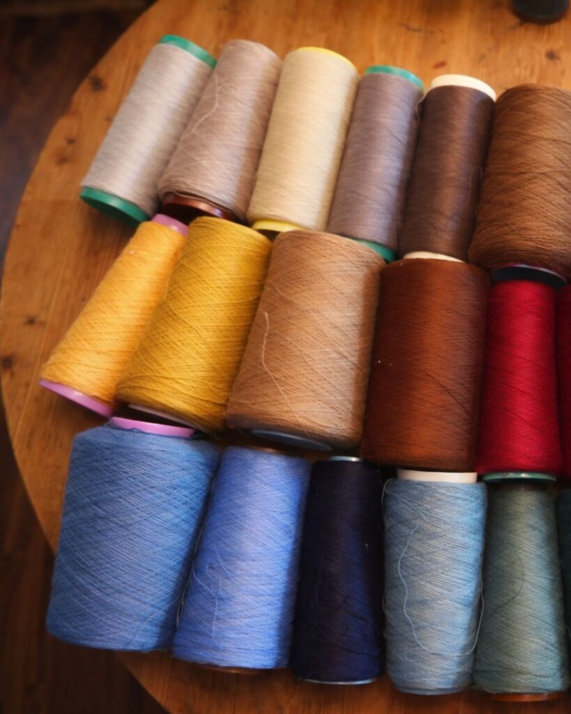 Garnkonen in Merinowolle in differenzierten Natur- und Farbtönen auf Holztisch im Atelier von Wiedengold.