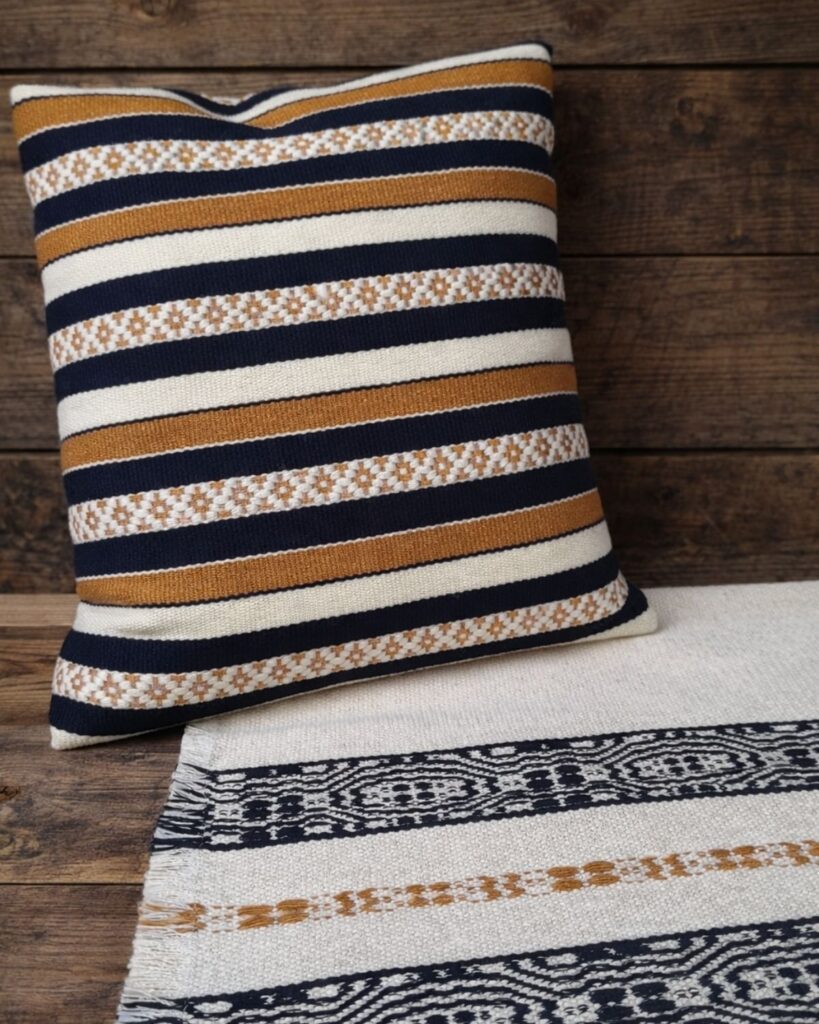 Handgewebte Kissen und Tischläufer aus Wolle und Viskose in Schwarz, Natur und Gold mit elegant-reduzierter Ornamentik.