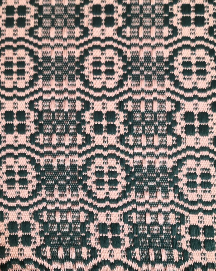 Detail eines handgewebten Webstoffes aus Naturmaterialien mit ornamentaler Musterung in Tannengrün und Weiß.